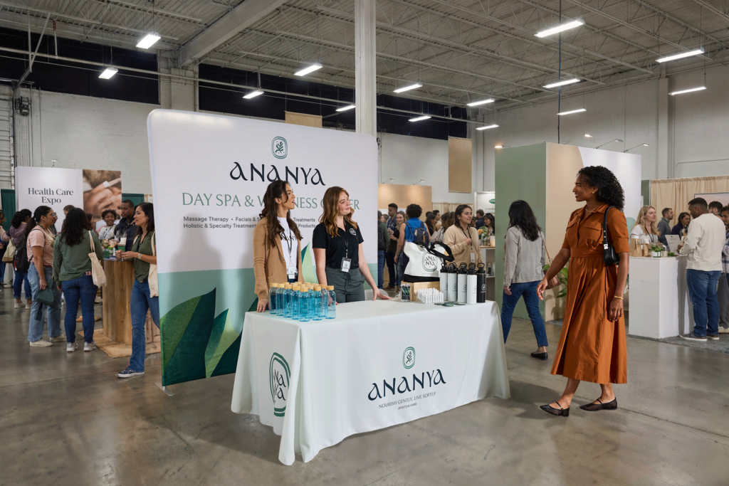 Ananya Day Spa & Wellness Center trade show booth, featuring a staff member and visitors at a health care expo.
